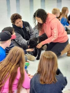 Dog rescues collaborate: Teacher and elementary students handling puppy